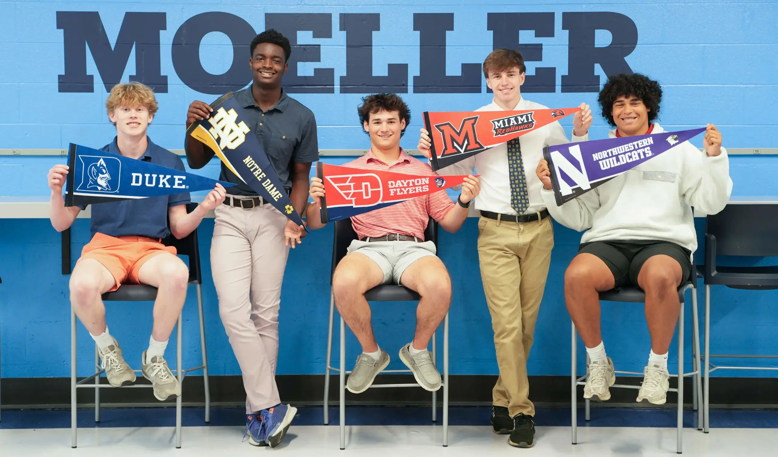 Moeller students holding flags, standing against blue wall